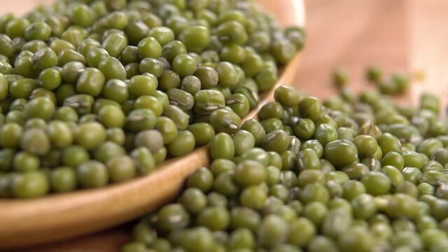 A full wooden spoon of green uncooked mung beans. Falling dry legumes in slow motion. Macro shot. Rustic view