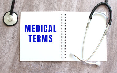 A white notebook with the words MEDICAL TERMS and a stethoscope on a gray wooden table.
