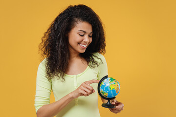 Fun african american young woman 20s wear green shirt hold in hands look at Earth world globe isolated on yellow background studio portrait. Stop nature garbage ecology environment protection concept