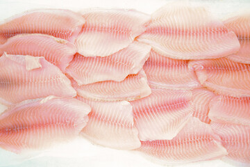 Butchered fish fillets are laid out (flat lay)  on ice on the  stalls (counter) of the grocery...