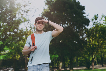 Young student man in blue t-shirt backpack hold hand at forehead look far away distance walk rest relax in spring green city park go down alley sunshine outside on nature Education high school concept