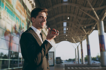 Bottom view happy traveler businessman young man in black suit stand outside at international airport terminal use mobile phone booking taxi order hotel record voice Air flight business trip concept.