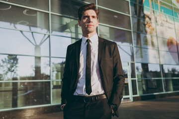 Bottom view serious young traveler brunet businessman man 20s in black classic tie suit standing outside at international airport terminal look aside People air flight business trip lifestyle concept