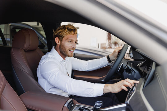 Happy man customer buyer client in classic suit shirt sit in car salon turn on music drive chooses auto wants buy new automobile in showroom vehicle dealership store motor show indoor Sales concept.