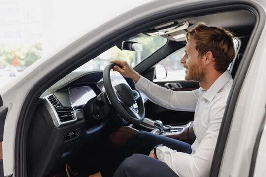 Side view man customer male buyer businessman client in classic suit sit in car salon chooses auto wants to buy new automobile in showroom vehicle dealership store motor show indoor Car sales concept