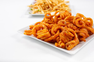 A view of a plate of curly fires, and a plate of common french fries in the background.