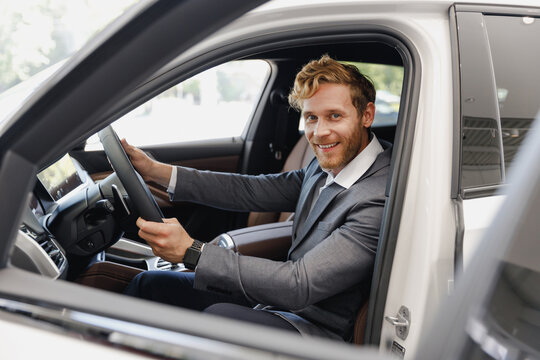 Smiling man happy customer male buyer client in classic grey suit driving car hold wheel choose auto want buy new automobile in showroom vehicle salon dealership store motor show indoor Sale concept