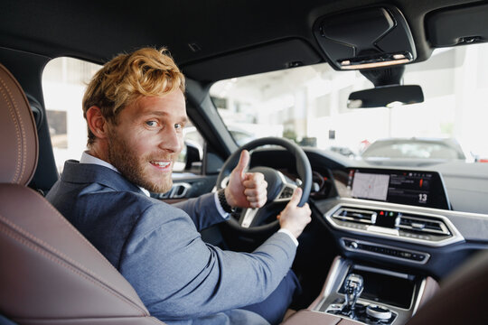 Serious businessman blond man driver male cabdriver in classic grey suit drive car hold wheel in traffic jam look camera show thumb up test auto want buy new automobile vehicle Sale transport concept.