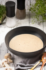 A champignon mushroom soup in a deep black bowl on a white wooden table