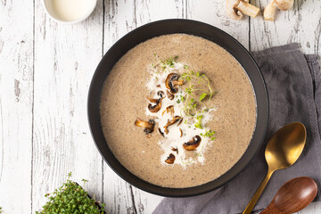A mushroom soup with thyme, sour cream and fried champignons in a deep black bowl on a white wooden table, top view