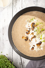 A mushroom soup with thyme, sour cream and fried champignons in a deep black bowl on a white wooden table, top view