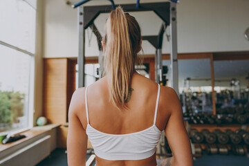 Back rear view caucasian young strong skinny sporty athletic sportswoman woman 20s wearing white sportswear warm up training do exercises in gym indoors. Workout sport motivation lifestyle concept