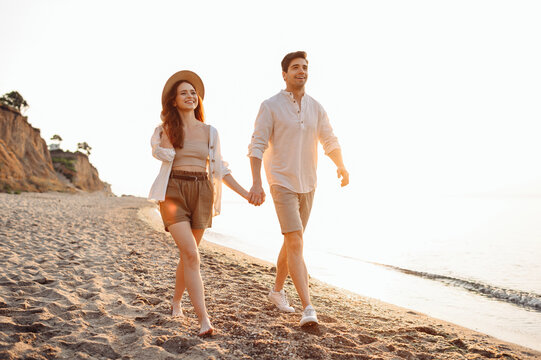 Full body smiling happy fun young couple two friends family man woman 20s wearing casual clothes hold hands walk together at sunrise over sea beach ocean outdoor exotic seaside in summer day evening.