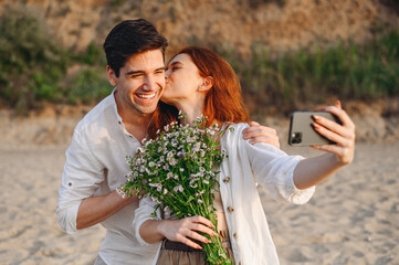 Young couple family man woman in white clothes rest together hold bouquet kiss do selfie shot...