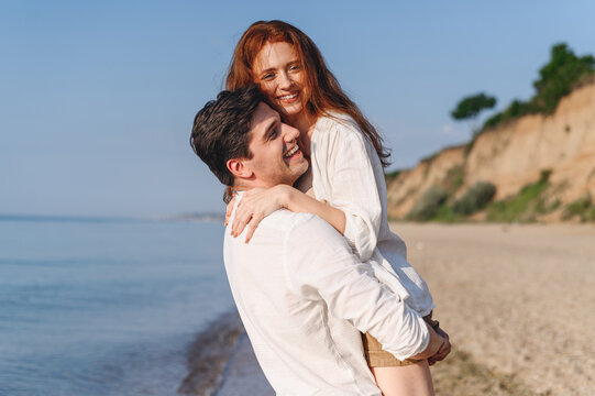 Side view smiling fun young couple two friends family man woman in white clothes boyfriend hug hold girlfriend at sunrise over sea sand beach ocean outdoor exotic seaside in summer day sunset evening.