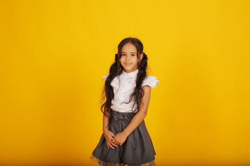 Naklejka premium a beautiful happy dark-skinned schoolgirl girl with dark hair in a school uniform, a gray skirt and a white blouse