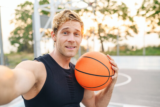 Close up happy cool young sporty sportsman man in black sports clothes training do selfie shot pov on mobile phone hold ball play at basketball game playground court Outdoor courtyard sport concept