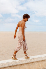 Afro latin girl walking along a beach wall in a summer dress