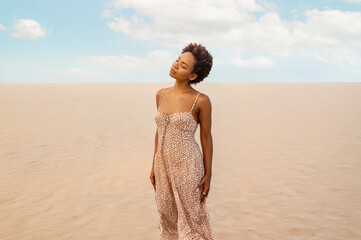 Girl with afro and summer clothes with her eyes closed in the sand. Concept of tranquility and...