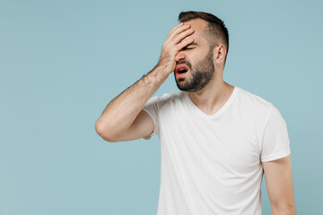 Fototapeta na wymiar Young shocked embarrassed dissatisfied man 20s in casual white t-shirt put hand on face facepalm epic fail mistaken omg gesture isolated on plain pastel light blue color background studio portrait