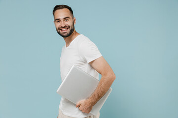 Side view young smiling happy man 20s in blank print design white t-shirt hold closed laptop pc...