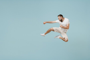 Full length young strong fighter caucasian man 20s in casual white t-shirt jump high do fighting gesture isolated on plain pastel light blue color background studio portrait. People lifestyle gesture.