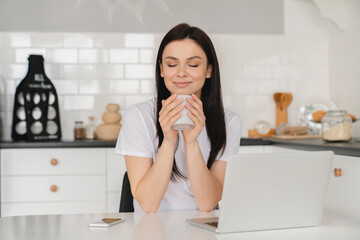 Young beautiful caucasian woman girl enjoying morning decaf coffee tea hot drink beverage at home kitchen. Female freelancer drinking for breakfast indoors for energy.