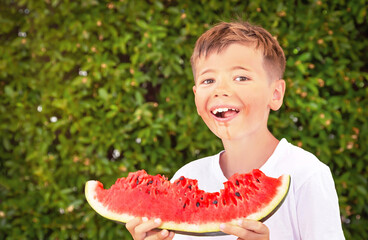 Happy child (boy) is eating a red juicy, tasty watermelon. Caucasian kid smiling and having fun. Concept of healthy food, happy childhood, summer vacation. Nature background. Copy space..