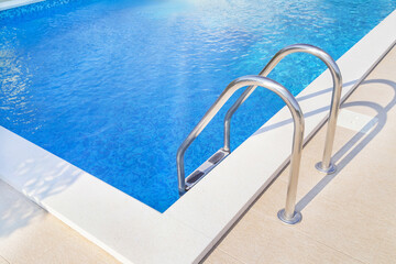 Close up of ladder stainless handrails (stairs) into the blue swimming pool. Vacation and sport...