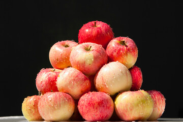 Melba apples. Ripe Melba apples in drops of water are stacked in a heap on a black background