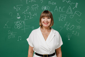 Happy teacher mature elderly senior elegant lady woman 55 years old wears shirt look camera isolated on green wall chalk blackboard background studio. Education in school September 1 concept.