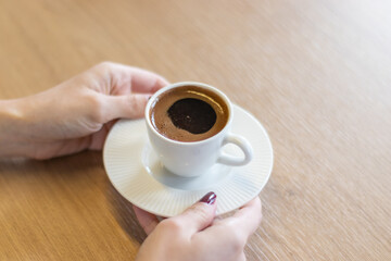 The woman on the wooden table holding Turkish coffee with your hands
