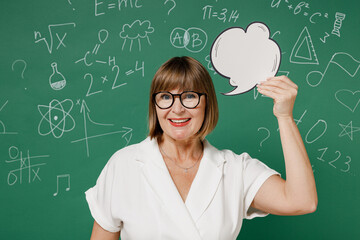 Dreamful teacher mature elderly lady woman 55 wear shirt glasses hold say cloud with lightbulb look camera isolated on green wall chalk blackboard background studio. Education in high school concept.