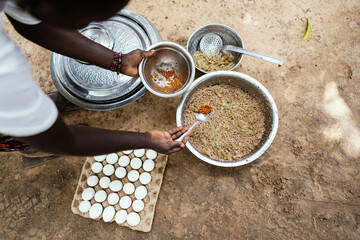 Black African cook adds spice to a simple dish she's preparing for her family, consisting only of...