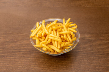 Glass bowl with large portion of classic French fries with salt on wooden table