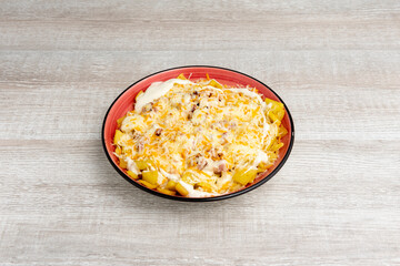 Portion of fried ranch potatoes with cheddar cheese, cream cheese and grated cheese with fried bacon on a red plate.