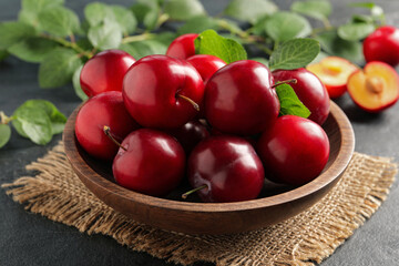Delicious ripe cherry plums with leaves on black table