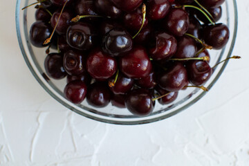 Glass bowl full of sweet cherries on a rough surface.