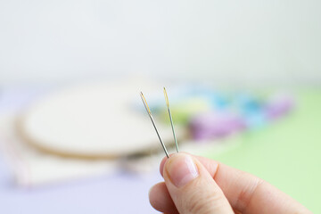 Two embroidery needles with a gilded eye of a needle in hand with a blurred background.
