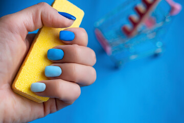 Women fingers with Beautiful Manicure in blue color holding nail file with shopping basket on blue background