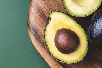 Half of avocado hass on wooden board on dark green background.