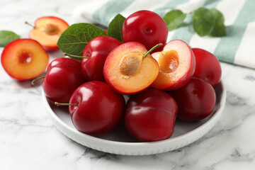 Delicious ripe cherry plums with leaves on white marble table