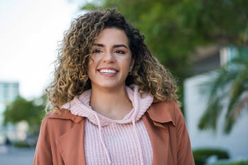 Latin woman smiling while standing outdoors on the street.