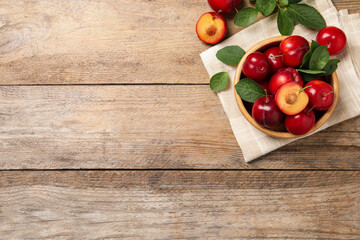 Delicious ripe cherry plums with leaves on wooden table, flat lay. Space for text