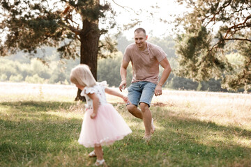 Father is playing with little daughter on summer day. Portrait dad with child together. Daddy, little daughter outdoors. Young father with baby girl walk in park. Family holiday in garden or forest.