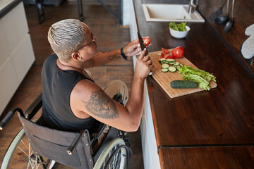 High angle portrait of contemporary tattooed woman with disability cooking dinner at home, copy...
