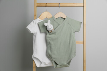 Baby bodysuits hanging on ladder near light wall