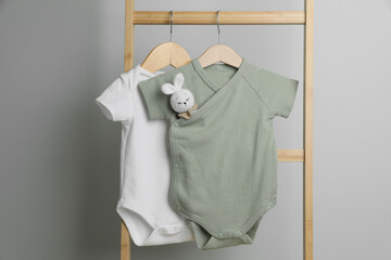 Baby bodysuits hanging on ladder near light wall
