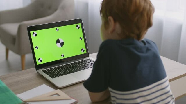Internet for kids. Tracking shot of little boy watching online movie on laptop with green chroma key screen