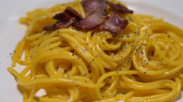 Spaghetti with carbonara, traditional pasta dish of Italian culture made with fresh egg yolk, original grated pecorino romano, crispy bacon and black pepper.